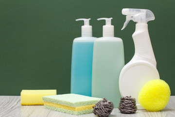 Bottles of dishwashing liquid, glass and tile cleaner and sponges on green background.