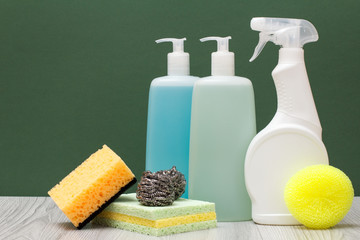 Bottles of dishwashing liquid, glass and tile cleaner and sponges on green background.