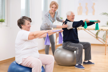 Elderly man and woman exercising on gymnastic balls during physiotherapy session at hospital
