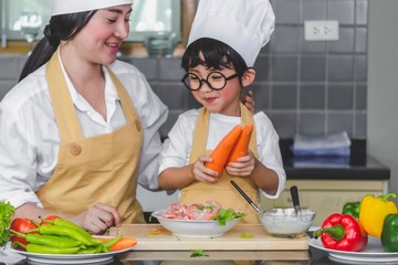 Asian woman young mother with son boy cooking salad food  with vegetable holding two carrots and tomatoes, bell peppers for happy family cook food enjoyment lifestyle kitchen