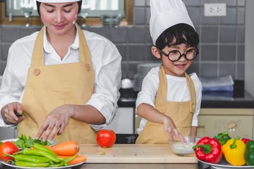 Asian woman young mother with son boy cooking salad mom sliced vegetables food son tasting salad dressing with vegetable carrots and tomatoes, bell peppers for happy family cook food enjoyment kitchen
