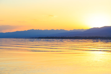 Beautiful sunset on a lake in the mountains. Kyrgyzstan, Issyk-Kul Lake. Bright sky, background in warm colors.