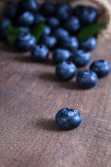 Close up blueberries on a wooden table with background is a pile of blueberries in a brown sack