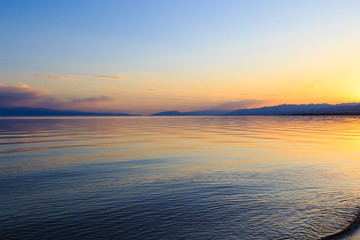 Beautiful sunset on a lake in the mountains. Kyrgyzstan, Issyk-Kul Lake. Bright sky, background in warm colors.