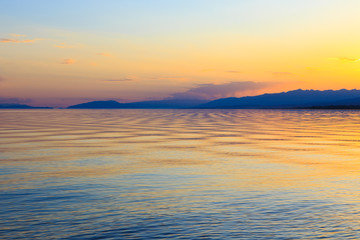 Beautiful sunset on a lake in the mountains. Kyrgyzstan, Issyk-Kul Lake. Bright sky, background in warm colors.