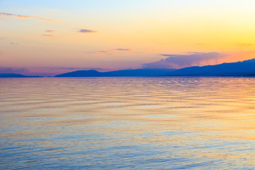 Beautiful sunset on a lake in the mountains. Kyrgyzstan, Issyk-Kul Lake. Bright sky, background in warm colors.