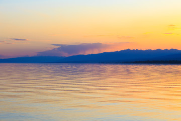 Beautiful sunset on a lake in the mountains. Kyrgyzstan, Issyk-Kul Lake. Bright sky, background in warm colors.