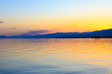 Beautiful sunset on a lake in the mountains. Kyrgyzstan, Issyk-Kul Lake. Bright sky, background in warm colors.