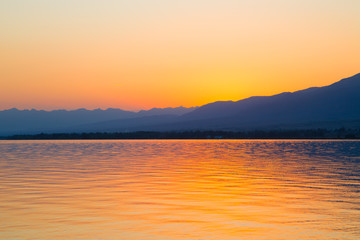 Beautiful sunset on a lake in the mountains. Kyrgyzstan, Issyk-Kul Lake. Bright sky, background in warm colors.