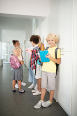 Boy with blue tablet standing near friends in school corridor