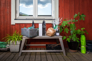 Outdoor front view of a gift present table bench with plants on a porch against red wooden plank wall and a window.