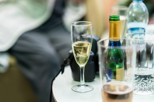 Candid snapshot of champagne glass and bottles on a small table. Traveler with camera taking a break resting with refreshments.