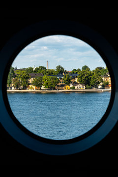 City summer landscape view of Stockholm seen from inside a ship cabin with round peep-hole window.