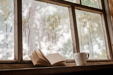 A white Cup and old books on the background of a rustic wooden wet window