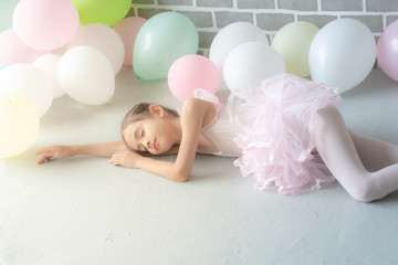 Obraz na płótnie Canvas Selective focus of relax little young girl ballet dancer in pink leotard and tutu sleeping on dance studio room floor with pastel colors balloon. Pretty child girl ballerina lying down on the floor