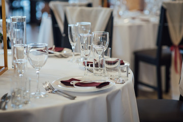 Glasses, flower fork, knife served for dinner in restaurant with cozy interior