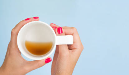 Flat lay mockup female hand with red manicure nails hold with an almost empty mug with coffee isolated on blue. Top view with copy space for banner
