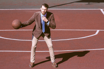 Attractive stylish bearded guy in a tie and jacket on the sports basketball court. A businessman goes in for sports and leads an active lifestyle. Sports break office worker. Lifestyle business man.