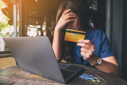 Closeup image of an Asian woman get stressed and broke while holding credit card with laptop on the table