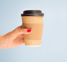 Female hand with red manicure holds disposable brown paper cup coffee. Mockup with copy space for a logo on a cup