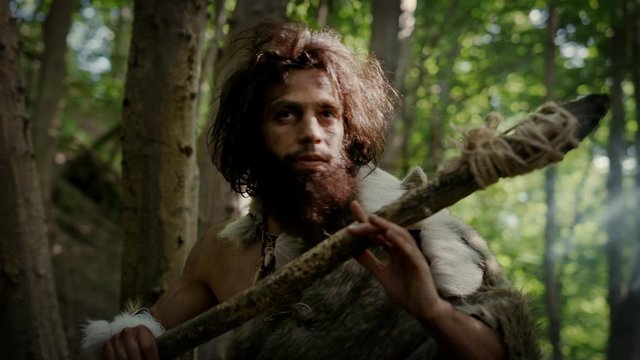Portrait of Primeval Caveman Wearing Animal Skin and Fur Hunting with a Stone Tipped Spear in the Prehistoric Forest. Prehistoric Neanderthal Hunter Ready to Throw Spear in the Jungle