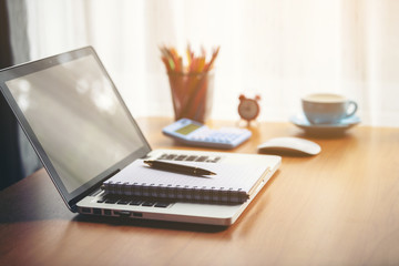 A coffee cup laptop with financial documents on a wooden table by the window.