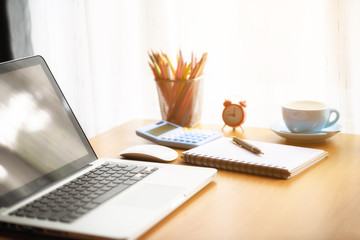 A coffee cup laptop with financial documents on a wooden table by the window.