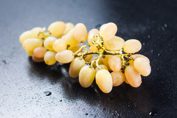 A bunch of homemade white grapes on a black background in drops of water.