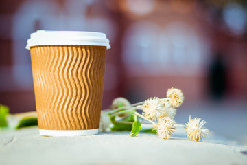 Paper cup with coffee. Dry flowers on brown background. Bright summer good morning. A bee flies near a coffee cup. Brown paper cup with plastic white lid.