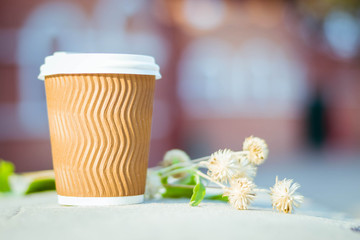 Paper cup with coffee. Dry flowers on brown background. Bright summer good morning. A bee flies near a coffee cup. Brown paper cup with plastic white lid.