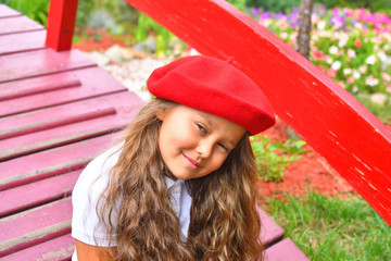 Portrait of a beautiful young Schoolgirl in red hat on the background park and red bridge