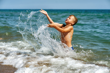 Happy boy playing with water in the sea . Active child at the seaside resort . Children's outdoor recreation