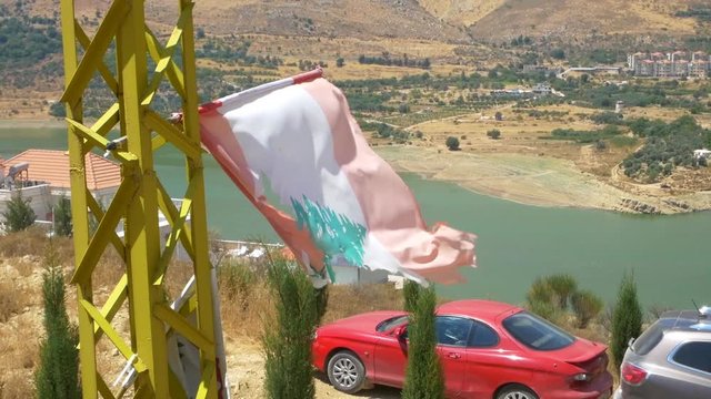 video of a broken Lebanon Flag waving in the wind with the background of a beautiful lake in Beeqa Valley, the most important agricultural region of Lebanon