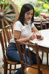 Cheerful asian young woman drinking warm tea enjoying it while sitting in cafe