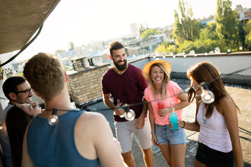 Young friends having fun at a rooftop party, playing the guitar, singing, dancing and drinking