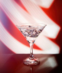 Martini glass isolated on a red background with stripes of neon light painting behind them. Light wave, play of colors, drawing with light.