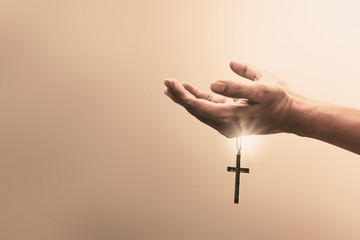 Praying hands hold a crucifix or cross of metal necklace with faith in religion and belief in God...
