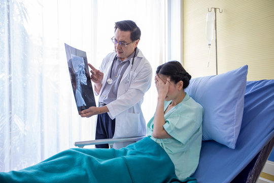 The doctor is explaining about the brain X-ray results to a female patient lying in bed at a hospital
