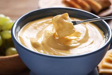 Dipping bread into pot with cheese fondue on table, closeup