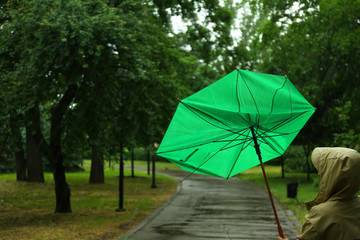 Woman with broken green umbrella in park on rainy day