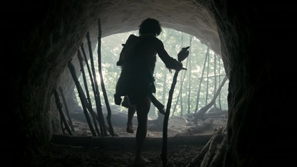 Primeval Caveman Wearing Animal Skin, Fur Holds Stone Tipped Spear Comes out of His Cave into Prehistoric Forest Ready to Hunt. Neanderthal Going Hunting into the Jungle. Following and Portrait Shot