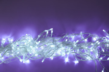 Glowing Christmas lights on dark violet background, top view. Space for text