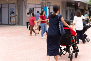 Fototapeta na wymiar Daughter pushing her mother in wheelchair walking along the shopping mall.