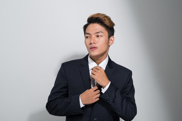 Asian businessman adjusting his necktie and wearing suit.