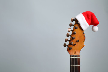 Guitar with Santa hat on grey background, space for text. Christmas music