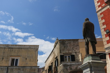 Bronze monument to Antonio Scialoja in a square in Procida. In the background the façades of the...