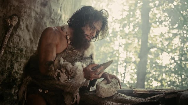 
Primeval Caveman Wearing Animal Skin Holds Sharp Stone and Makes First Primitive Tool for Hunting Animal Prey, or to Handle Hides. Neanderthal Using Handax. Dawn of Human Civilization
