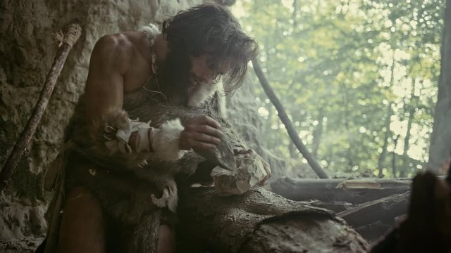 
Primeval Caveman Wearing Animal Skin Hits Rock with Sharp Stone and Makes First Primitive Tool for Hunting Animal Prey or to Handle Hides. Neanderthal Using Handax. Dawn of Human Civilization