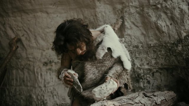 Primeval Caveman Wearing Animal Skin Hits Rock with Sharp Stone and Makes Primitive Tool for Hunting Animal Prey. Neanderthal Using Flint Rock to Create first Wheel. Slow Motion Shot