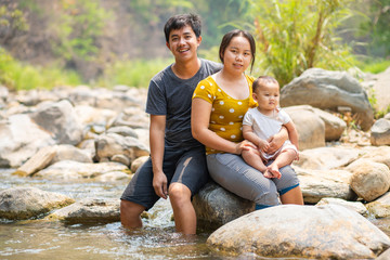 Asian Family sitting on rock in river on the day going for outdoor travelling
